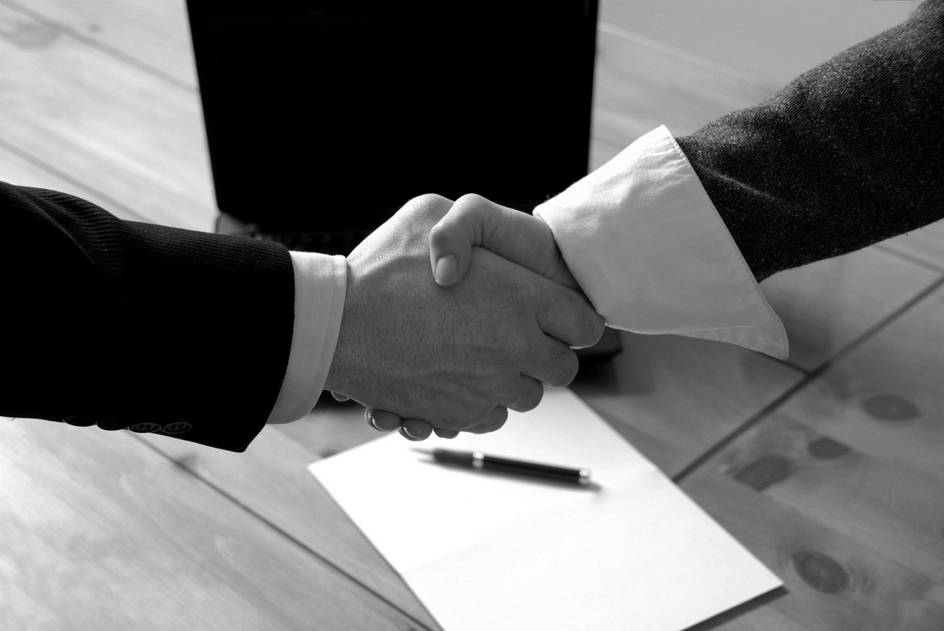 man and woman shaking hands in front of laptop